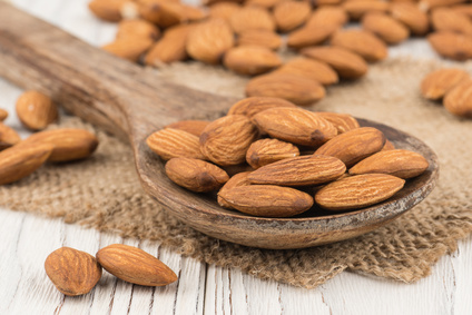 Almonds in a wooden spoon on the old white wooden table.