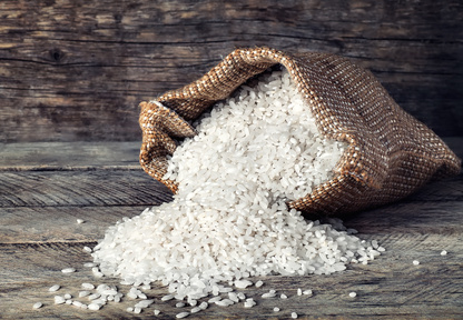 Raw grains of white rice in burlap bag on wooden background